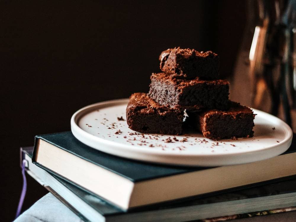 Delicious chocolate brownies stacked on a white plate, placed on top of a closed book, perfect for b.